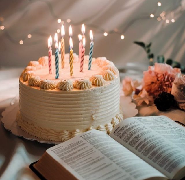 A beautiful birthday cake with glowing candles against a soft background with subtle light rays, an open Bible visible
