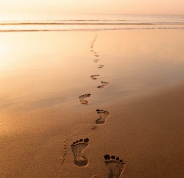 Two sets of footprints in sand at sunset, one set fading to single tracks, golden ethereal light, peaceful beach scene